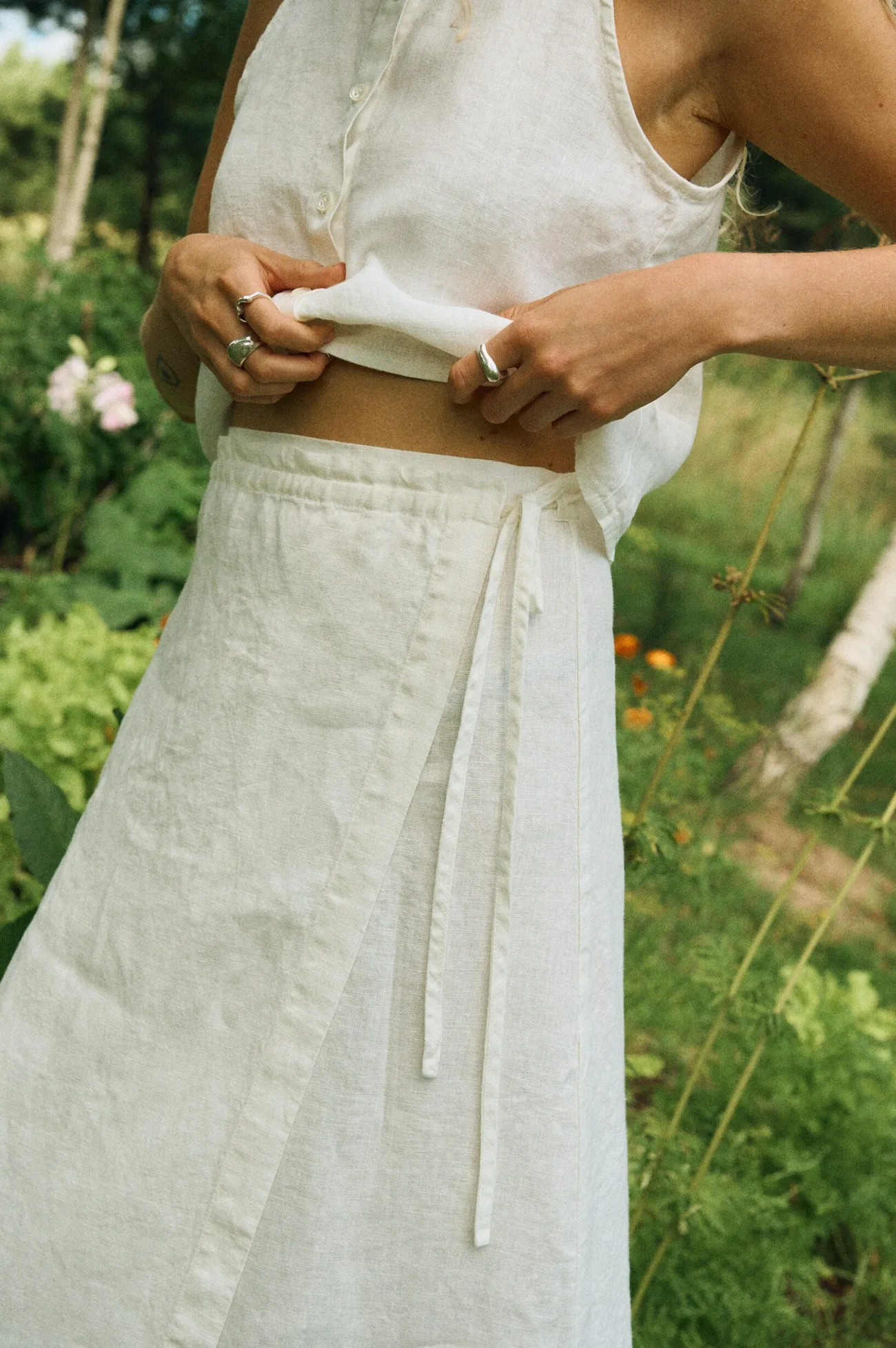 Close-up of a milky white linen wrap skirt with thin tie closure, paired with a matching sleeveless button-up crop top