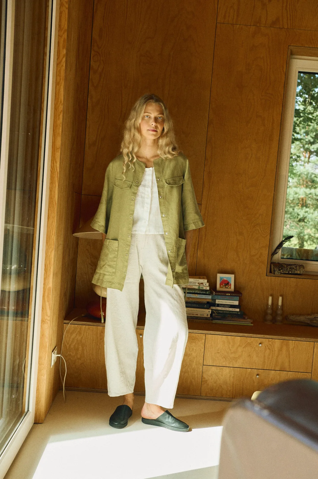 Woman wearing an olive green belted linen overshirt made from heavy linen, styled over a white sleeveless top and white wide-leg linen-cotton pants