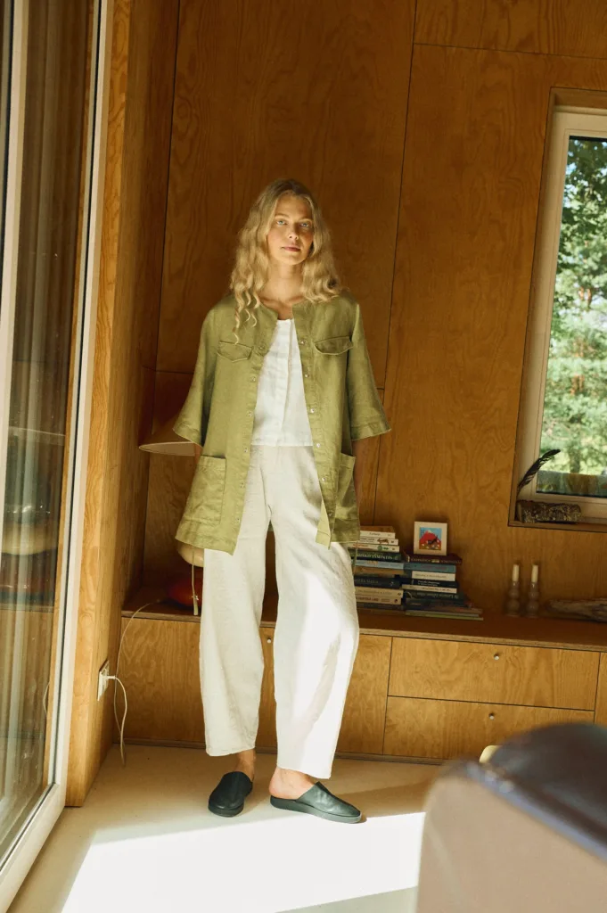 Woman wearing an olive green belted linen overshirt made from heavy linen, styled over a white sleeveless top and white wide-leg linen-cotton pants