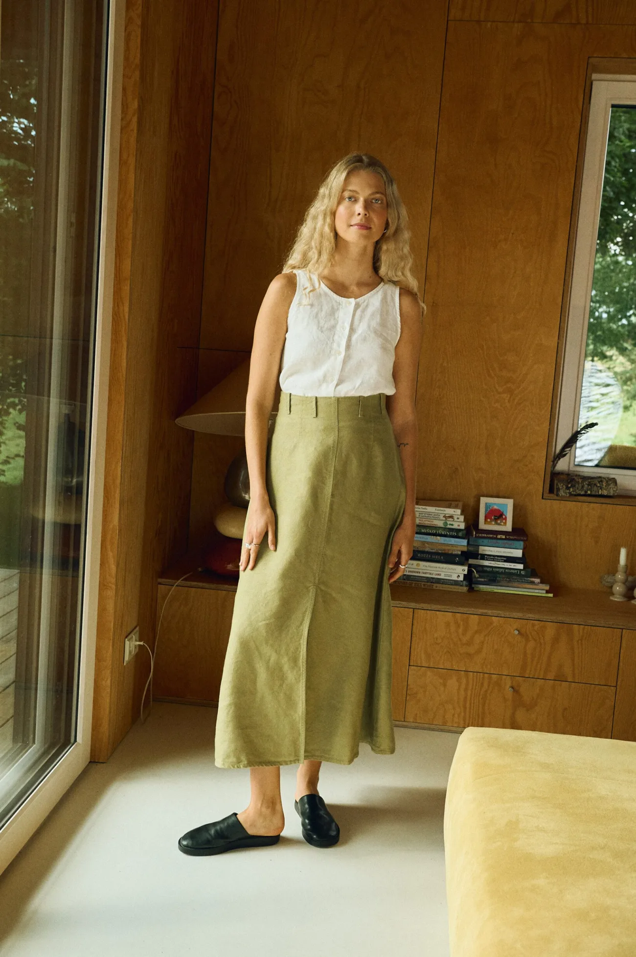 Woman wearing a high-waisted A-line midi skirt in heavy olive linen paired with a sleeveless white linen button-up top