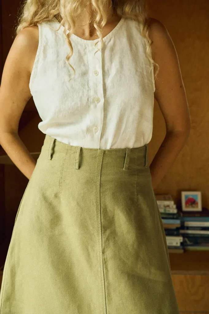 Close-up of a sleeveless white linen button-up top paired with a high-waisted olive green midi skirt made from heavy linen, featuring belt loops and a structured A-line silhouette