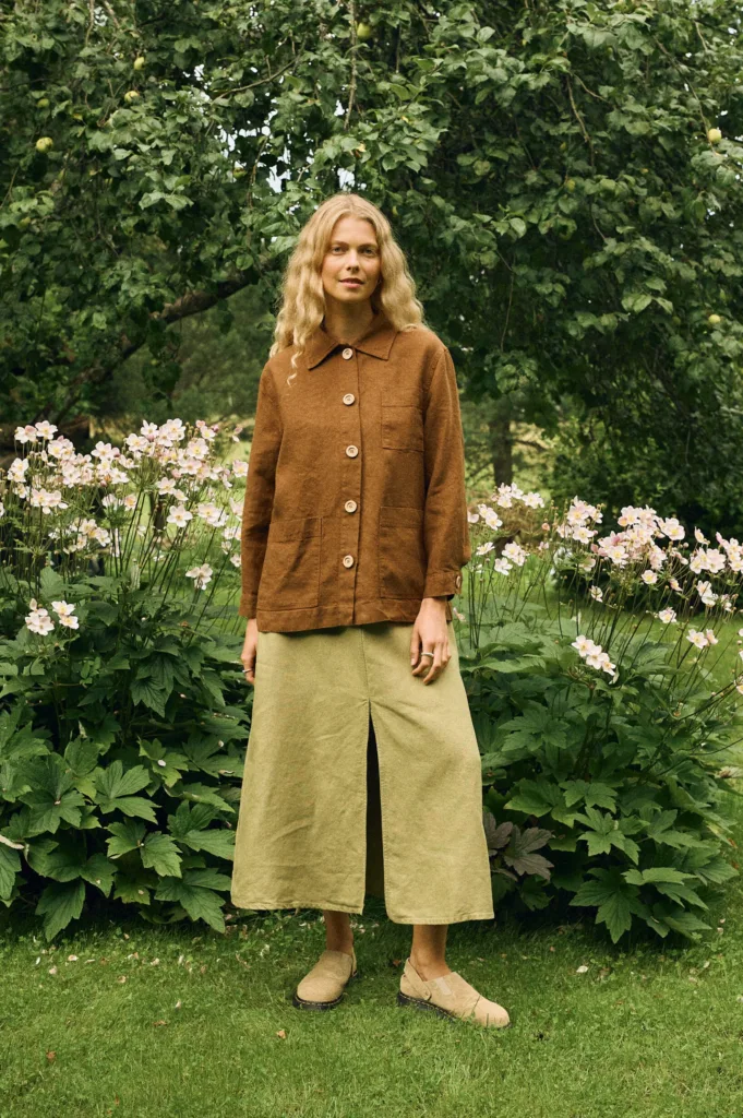 Woman wearing a brown linen-wool blend jacket with large buttons and patch pockets, styled with a high-waisted olive green heavy linen midi skirt featuring a front slit