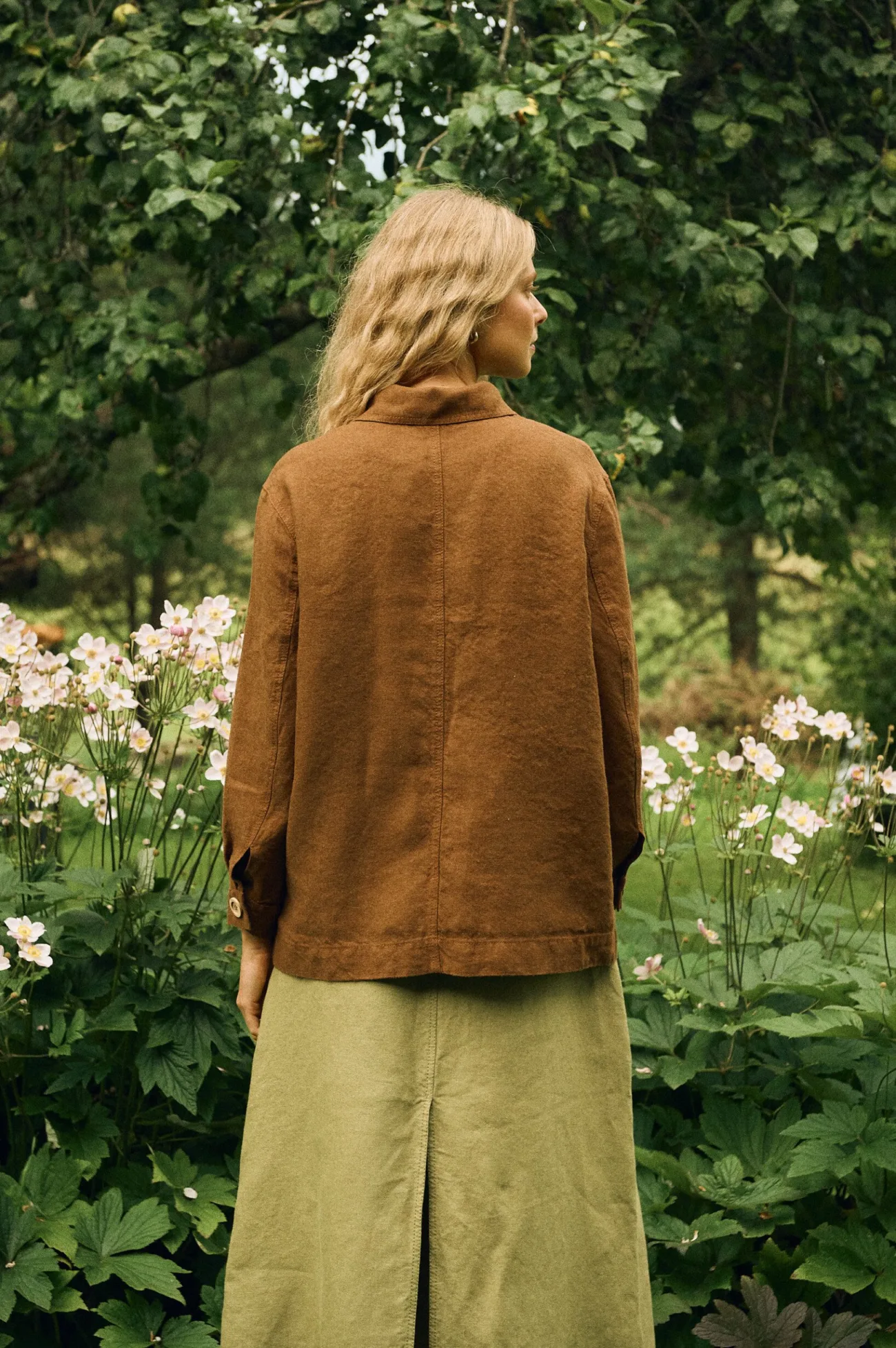 Back view of a warm brown linen-wool jacket, paired with a heavy linen A-line skirt in muted olive green with front and back slits