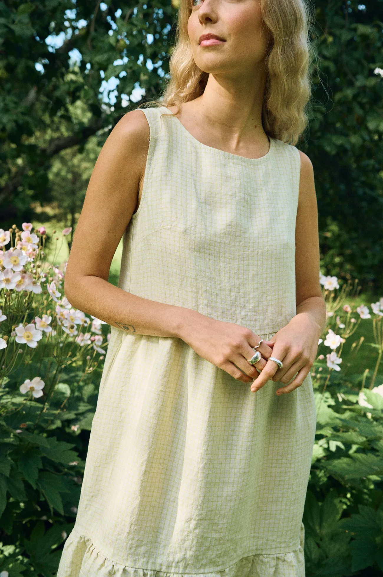 Close-up of a sleeveless midi dress in apple checks linen, featuring a round neckline, relaxed bodice, and gathered tiered skirt