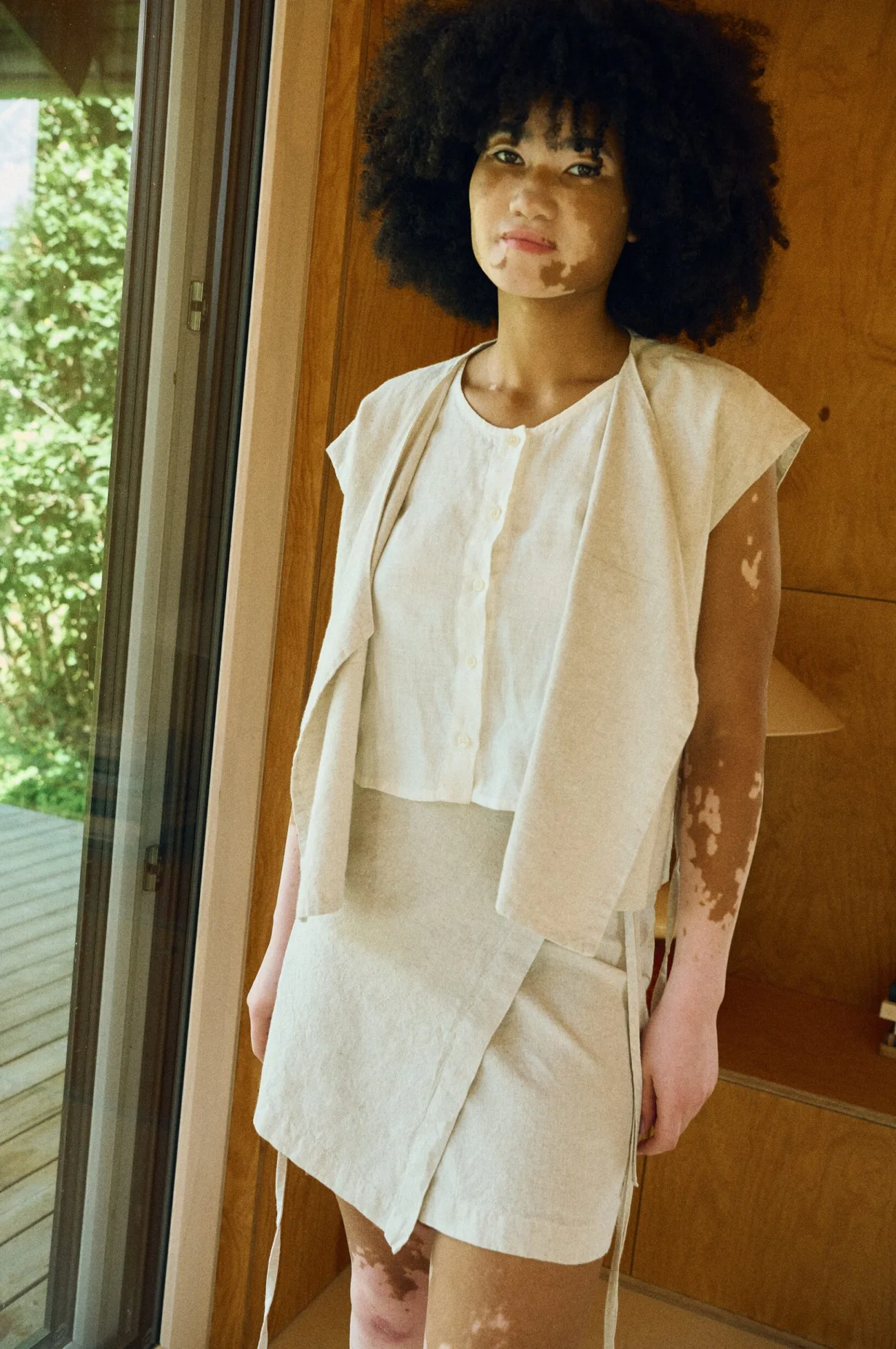 Model wearing a milky white linen sleeveless top paired with a natural linen-cotton blend vest and a matching linen-cotton blend wrap mini skirt
