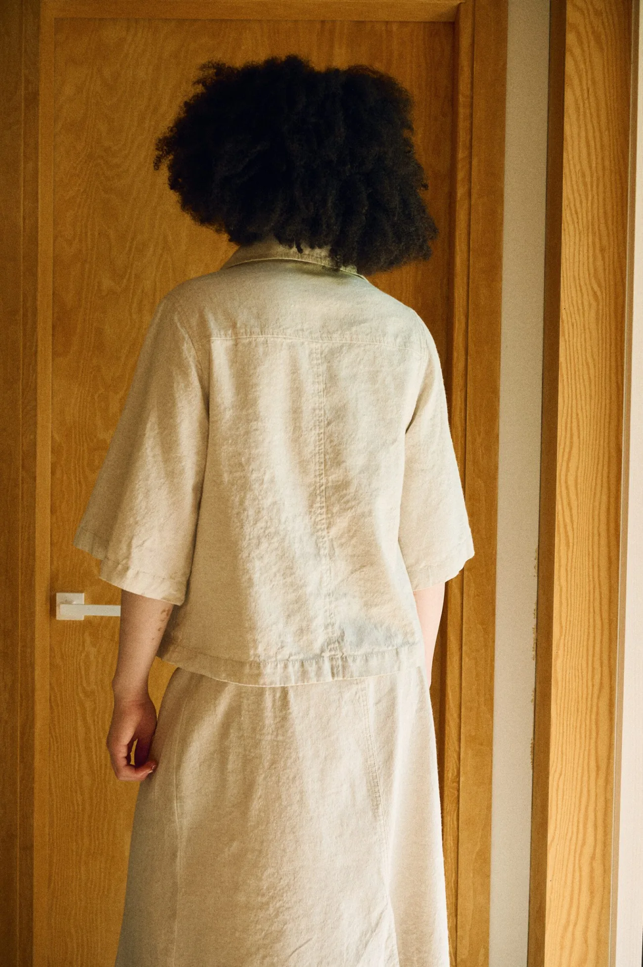 Rear view of a natural linen-cotton outfit showcasing a relaxed short-sleeve shirt with a classic collar, paired with a matching high-waisted midi skirt