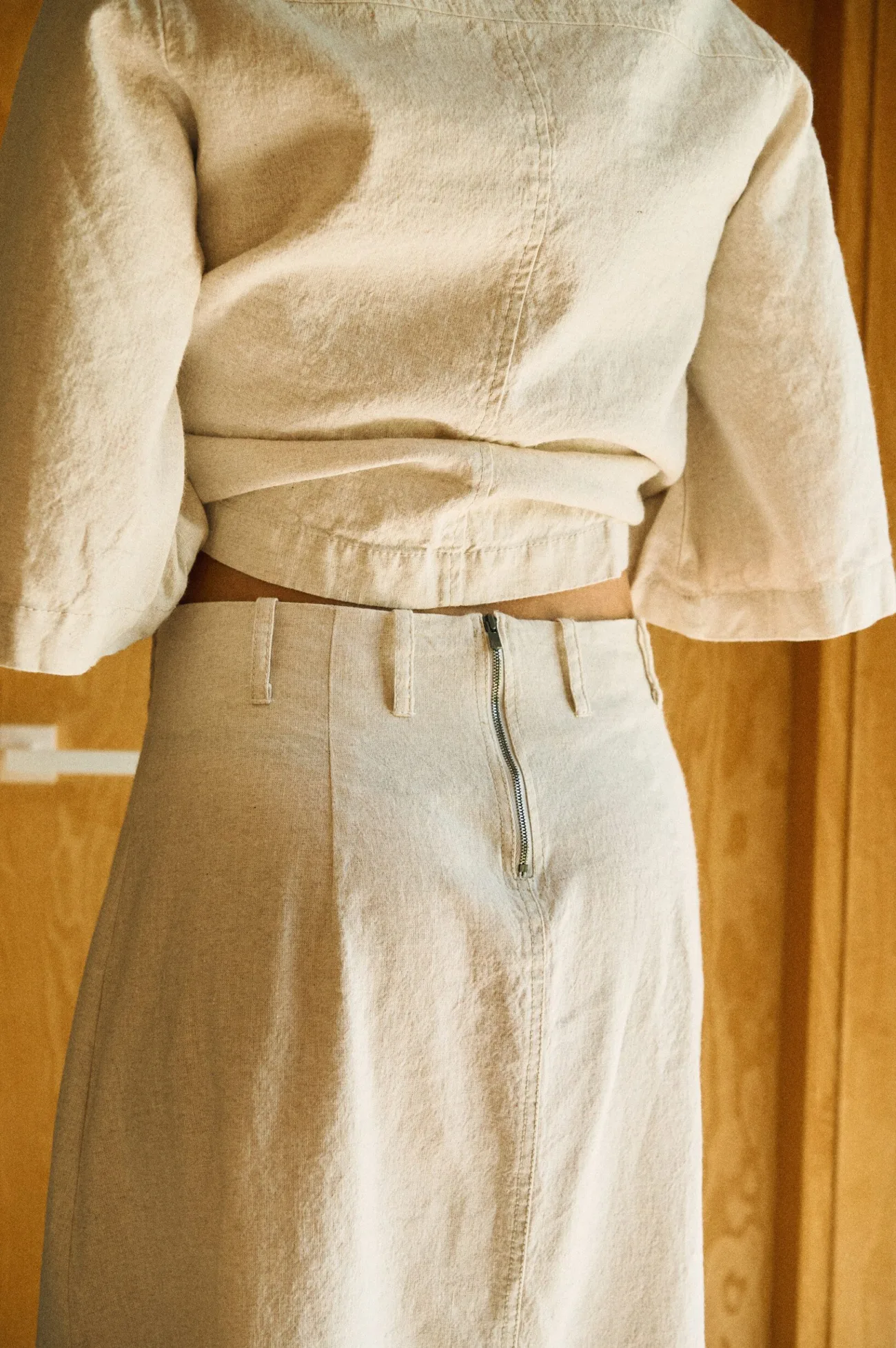 Close-up of the back of a natural-colored linen-cotton blend outfit, highlighting the exposed zipper detail on the high-waisted skirt