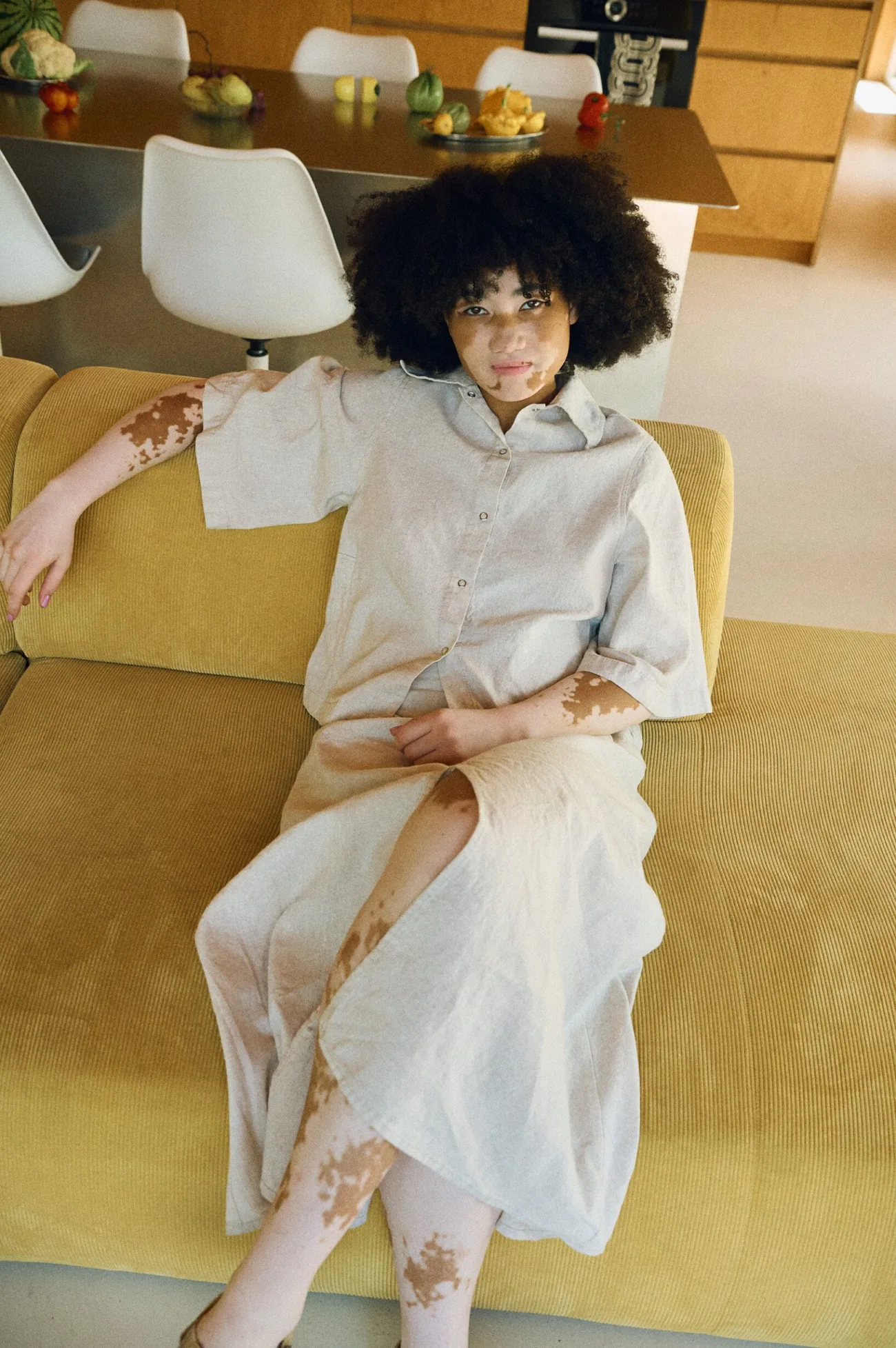 Woman lounging wearing a coordinated natural-colored linen-cotton blend set, featuring a relaxed button-up shirt and a midi skirt with a front slit