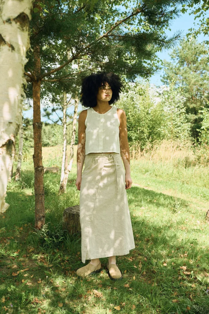 Woman wearing a natural cotton-linen blend wrap skirt with long adjustable ties and a clean A-line silhouette, styled with a sleeveless white linen button-up top
