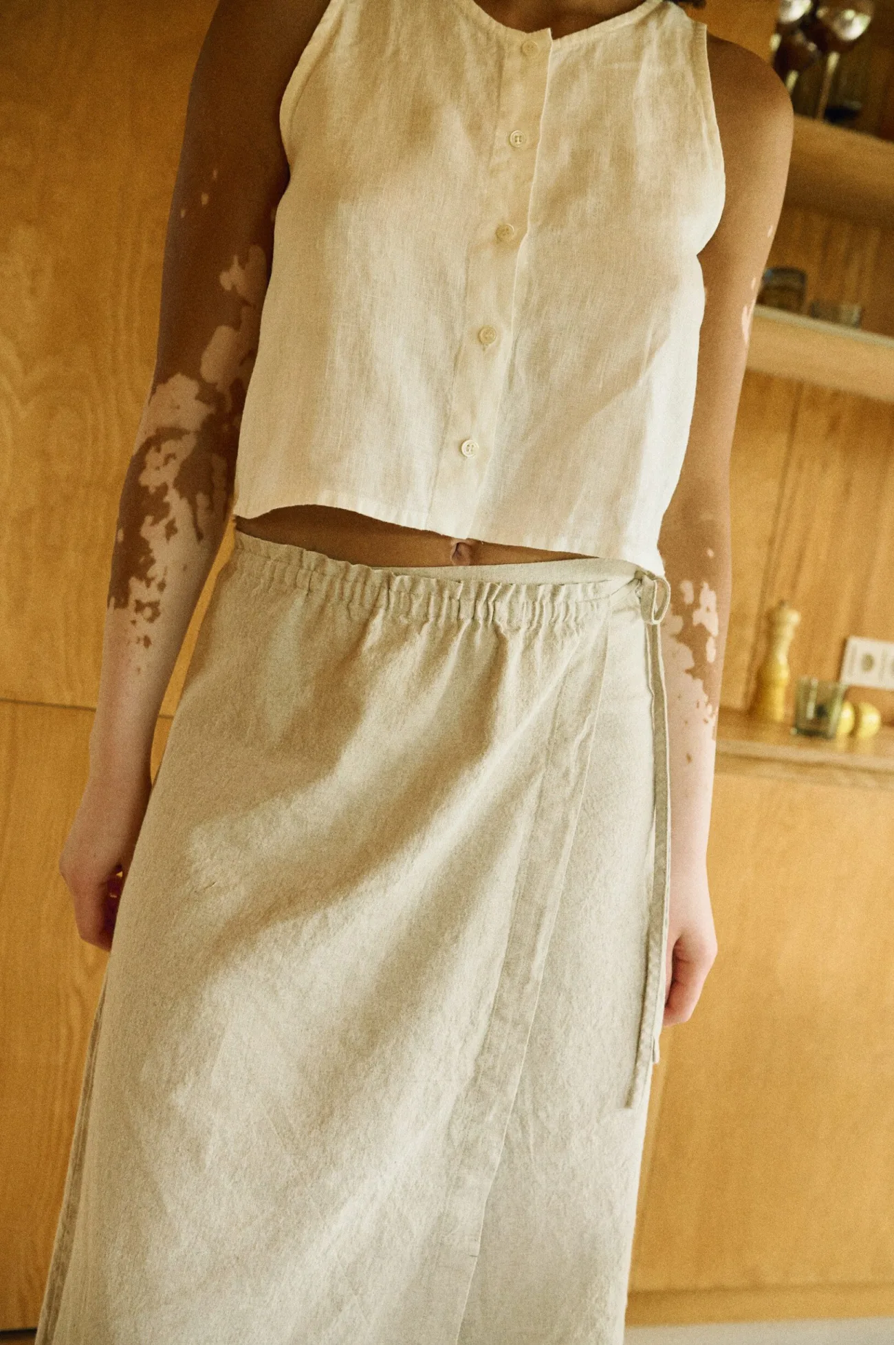 Close-up of a natural cotton-linen blend wrap skirt with a clean A-line silhouette, flat front waistband, and adjustable tie closure, paired with a sleeveless button-up linen top