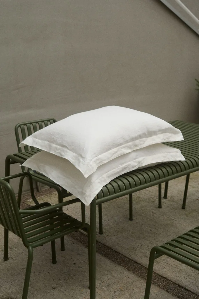 Two crisp milky white linen pillowcases stacked neatly on a green outdoor table, showcasing the natural texture and breathability of high-quality linen