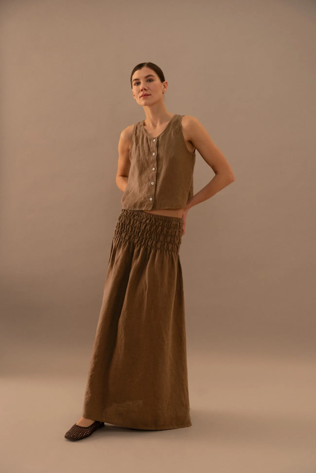 Cacao brown medium weight linen two-piece set for women featuring a sleeveless button front top and high waisted smocked maxi skirt