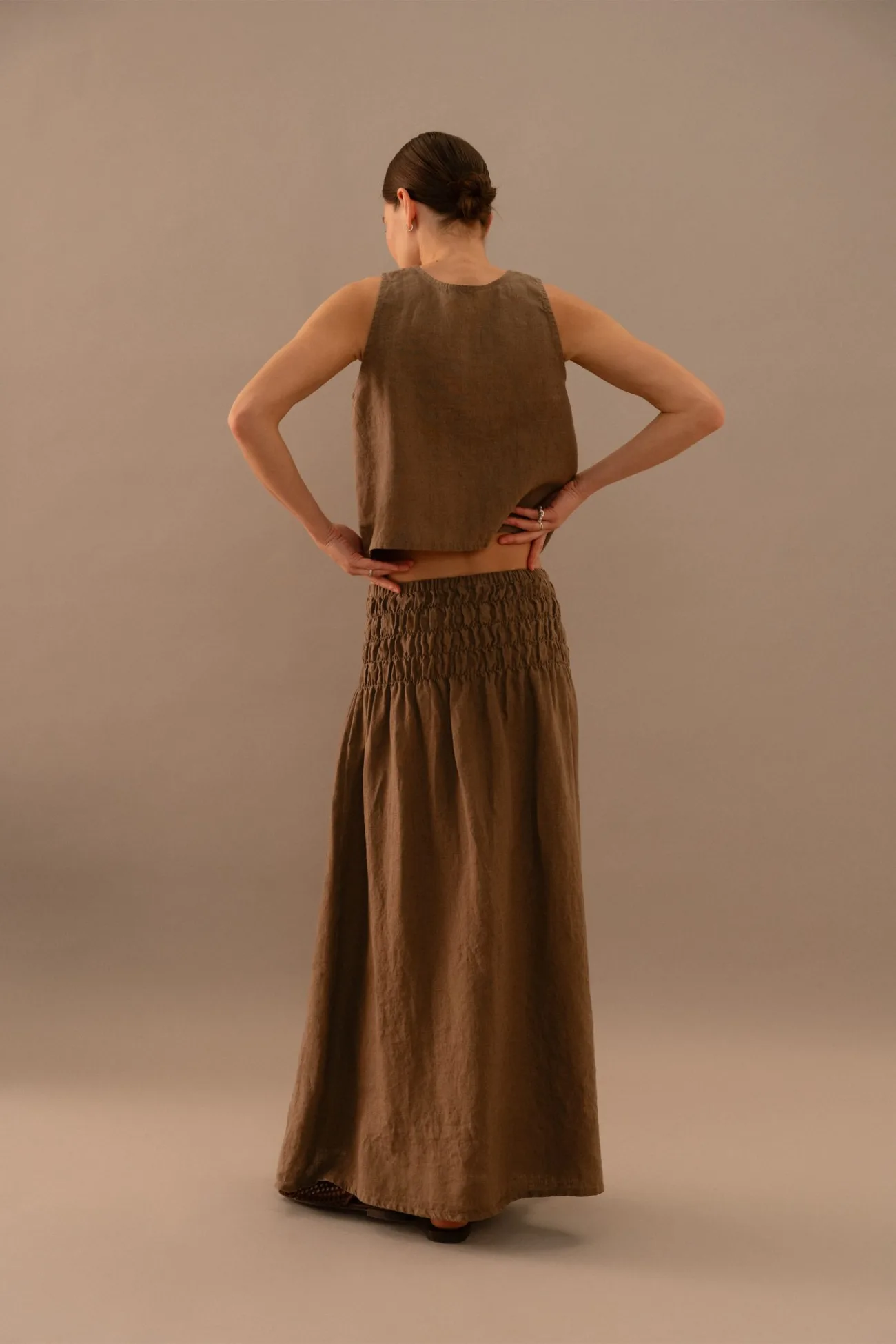 Back view of cacao brown medium weight linen two piece set for women featuring a sleeveless linen top and smocked maxi skirt