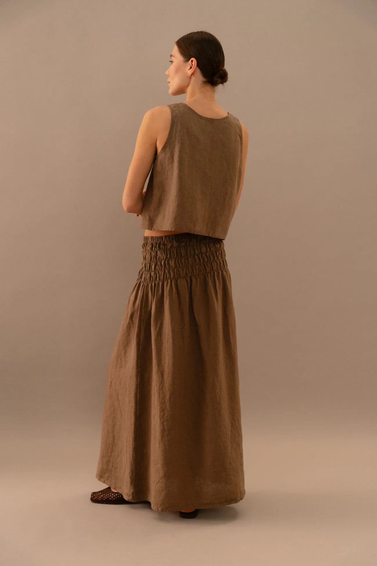 Back view of cacao linen maxi skirt with wide smocked elastic waistband and sleeveless matching top