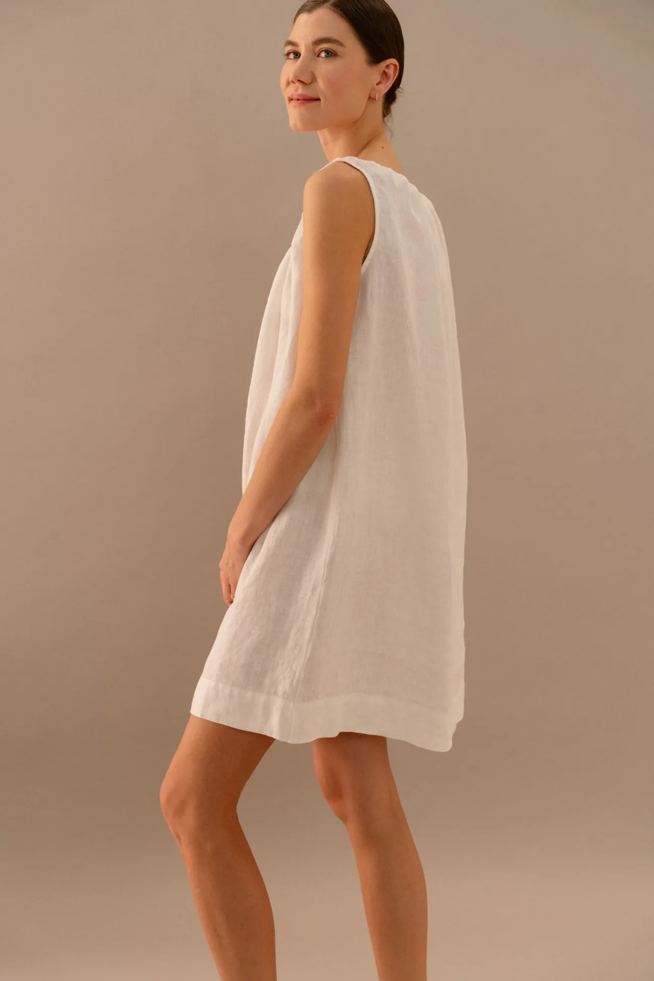Side view of white linen sleeveless dress with lightweight drape and above knee length