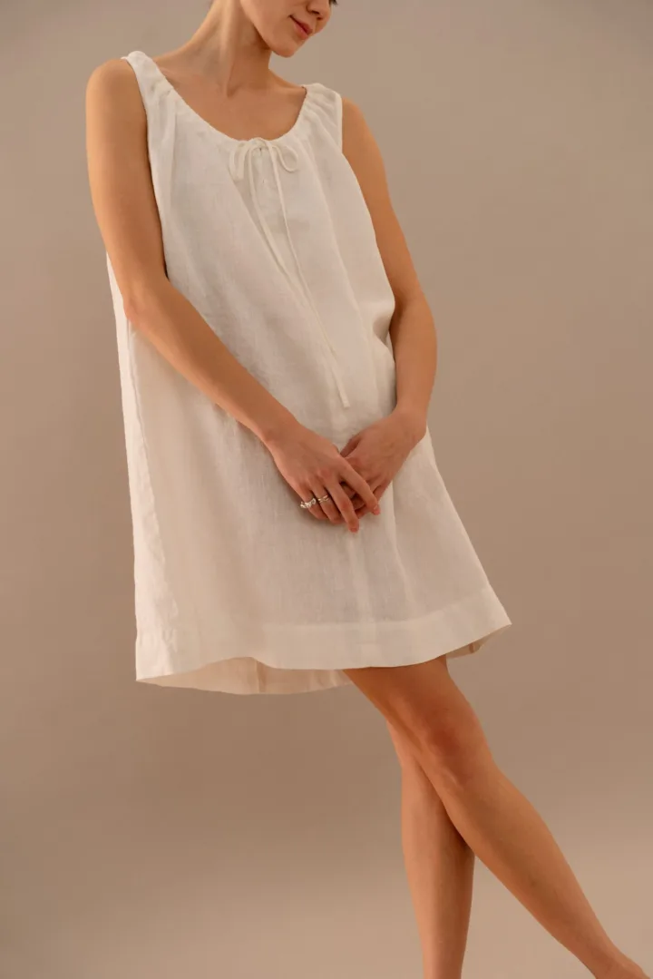 Close-up of white linen dress featuring gathered neckline and bow tie closure