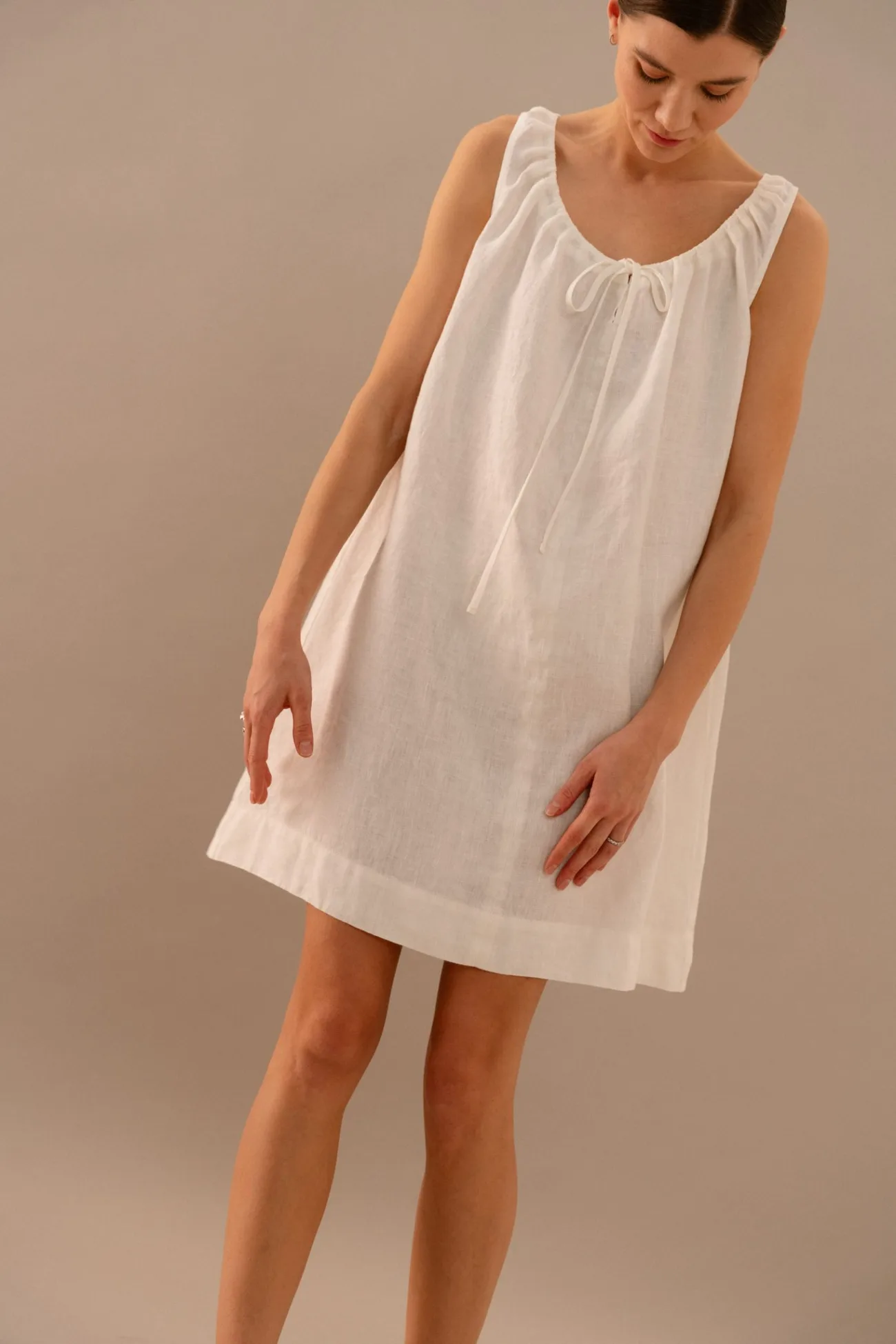White linen sleeveless mini dress with gathered neckline and adjustable tie detail