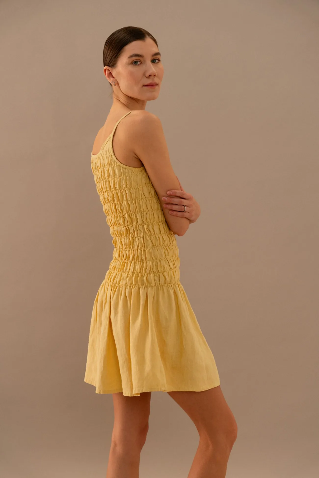 Butter linen sleeveless mini dress with textured smocked bodice, angled back view