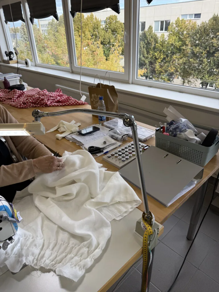 Seamstress working with milky white linen fabric at sewing workstation in Linenfox studio