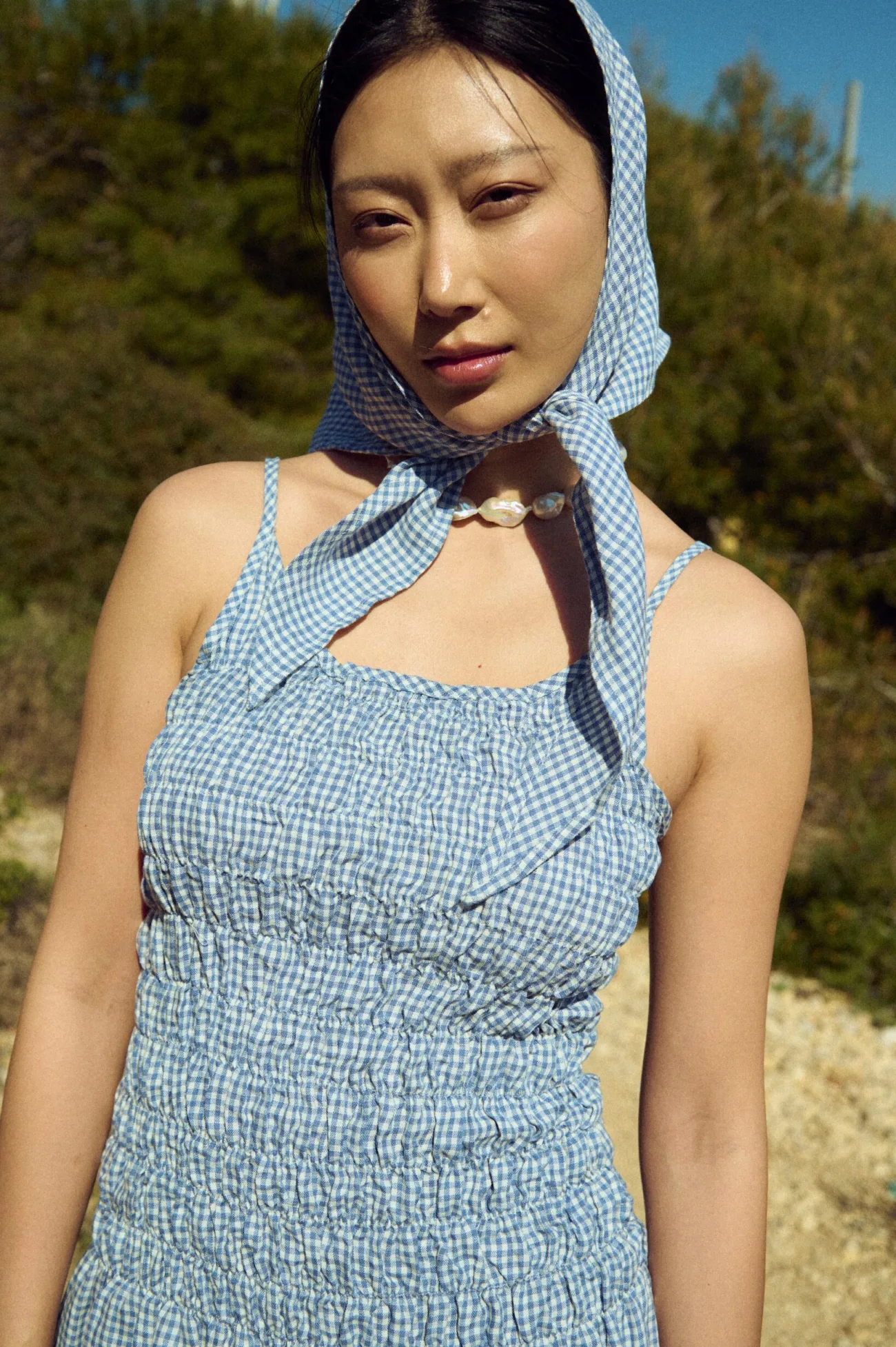 Close-up of a dusty blue mini gingham linen smocked mini dress with thin straps, styled with a matching gingham headscarf
