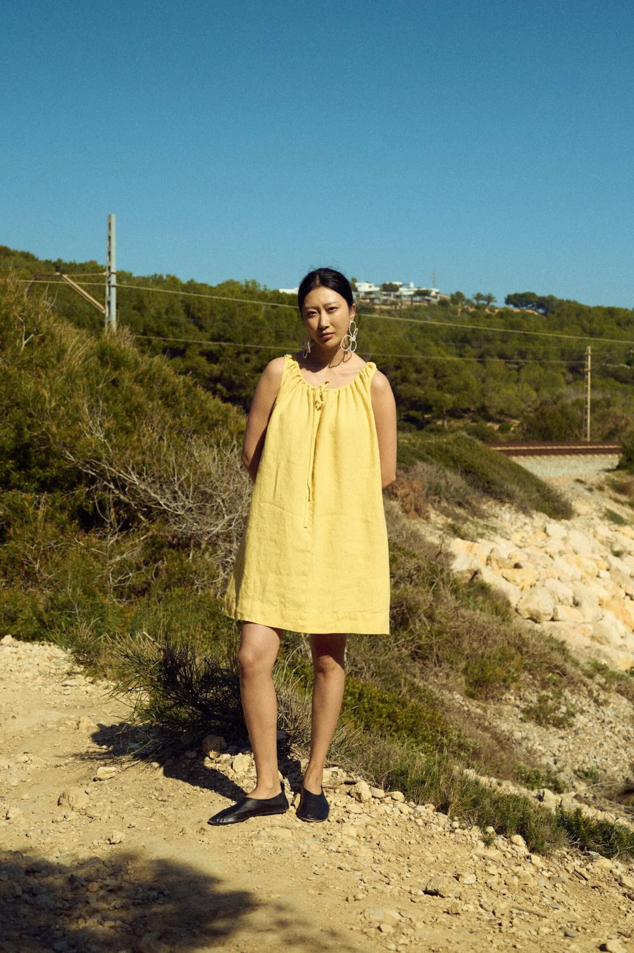 Woman wearing a sleeveless butter yellow linen mini dress with a gathered tie neckline and loose above-knee silhouette, shown from the front