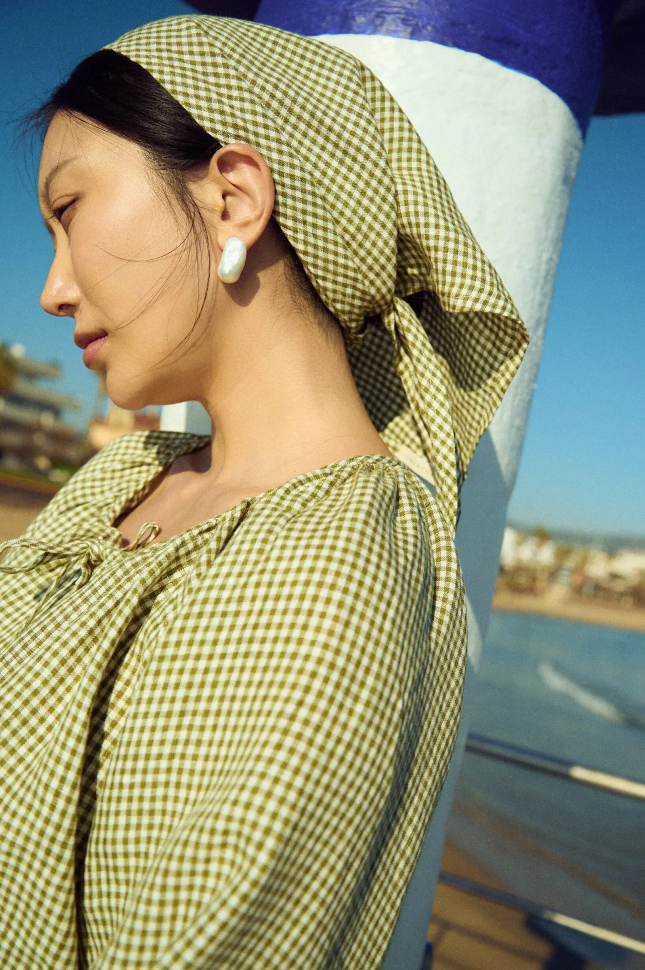 Close-up of a moss green mini gingham triangle headscarf tied at the back, styled with a matching gingham blouse