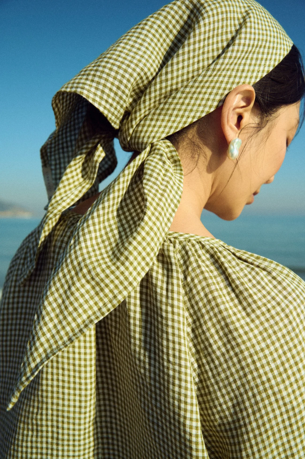 Moss green mini gingham triangle scarf tied at the nape, paired with a softly gathered gingham blouse