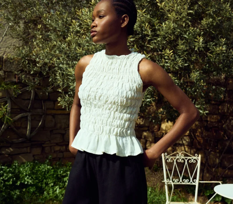 White linen smocked sleeveless top with gathered texture and ruffled hem, paired with black linen culottes