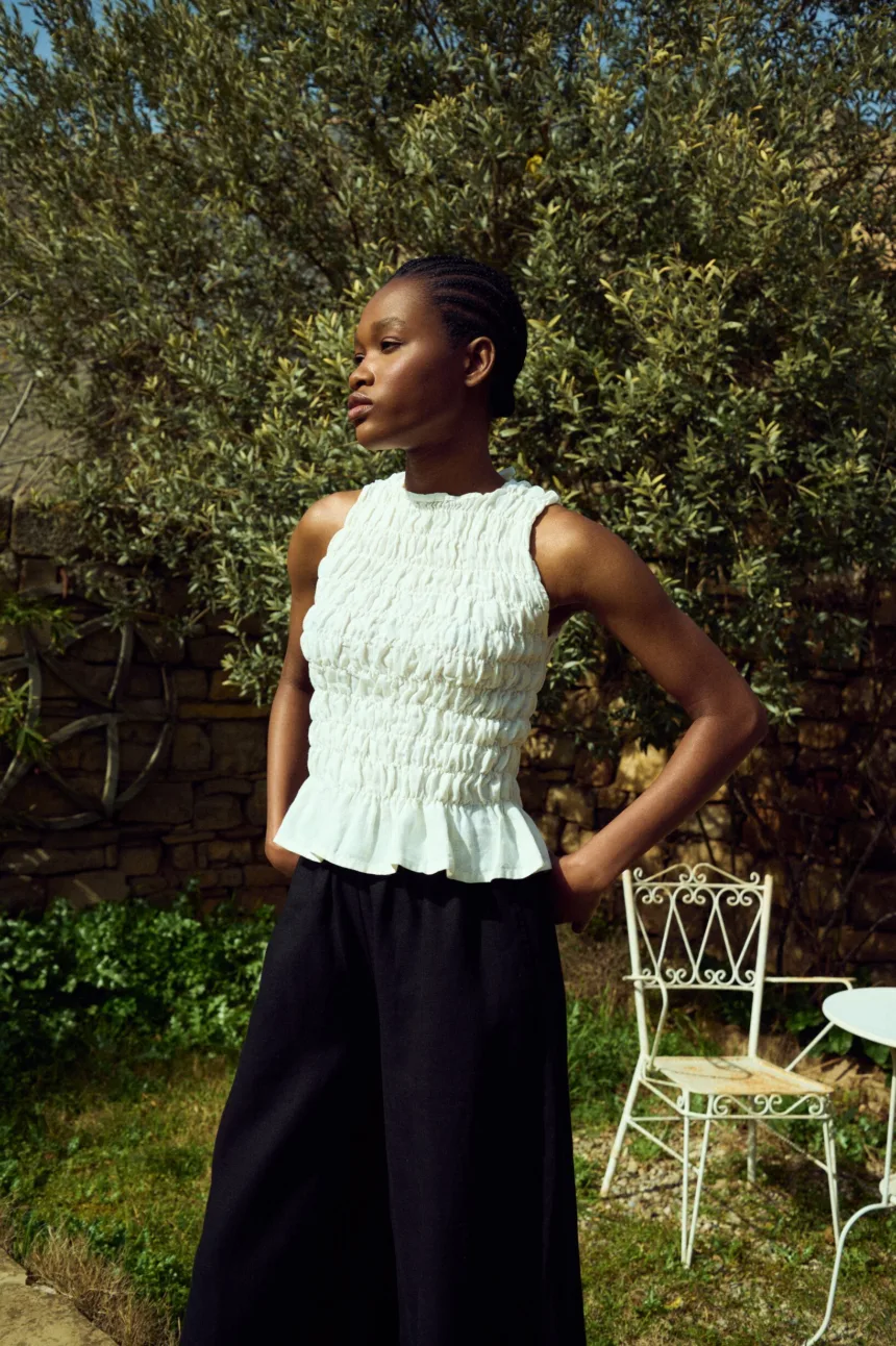 White linen smocked sleeveless top with gathered texture and ruffled hem, paired with black linen culottes
