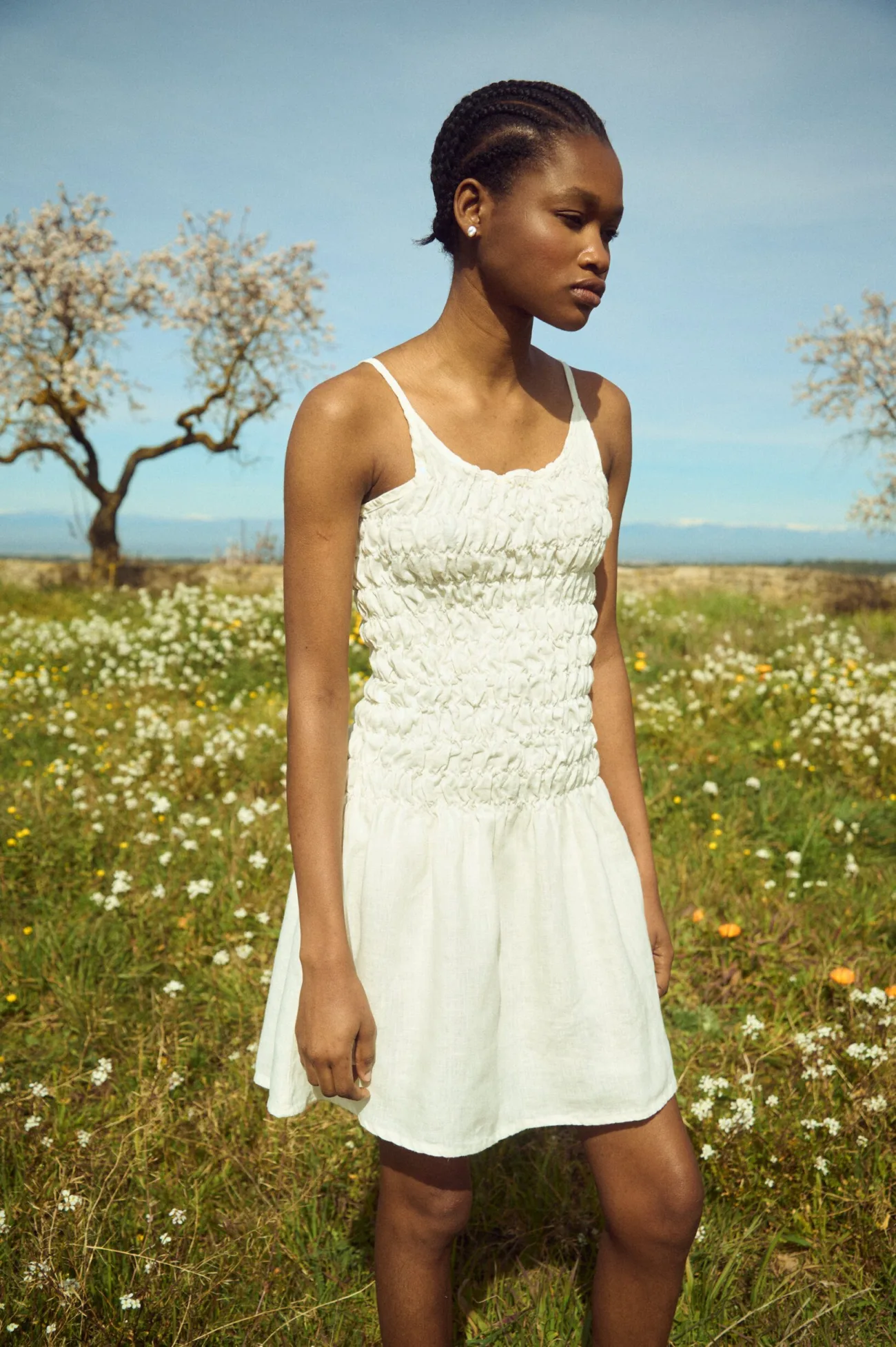 Front view of a milky white linen mini dress with thin straps and a smocked bodice