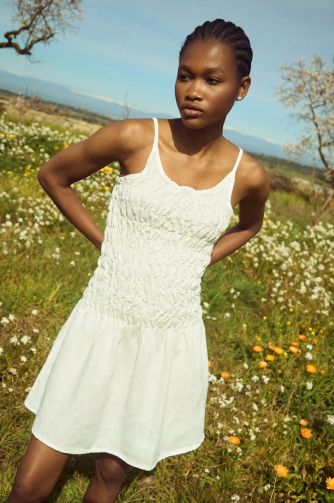 Milky white linen mini dress with thin straps, a textured smocked bodice, and a softly flared skirt
