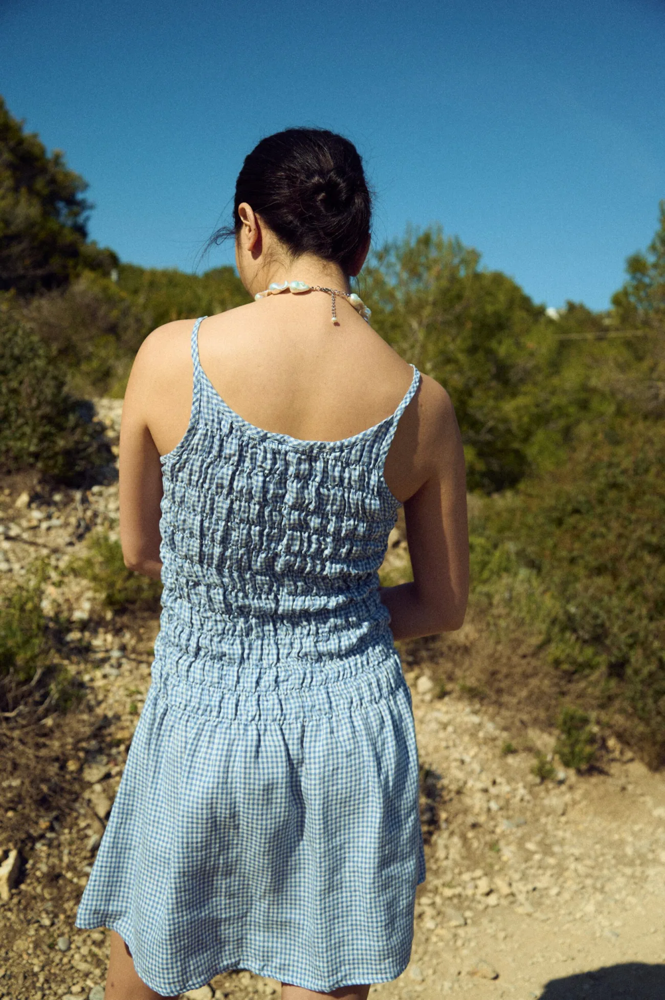 Back view of a light blue mini gingham dress with a ruched bodice and thin straps