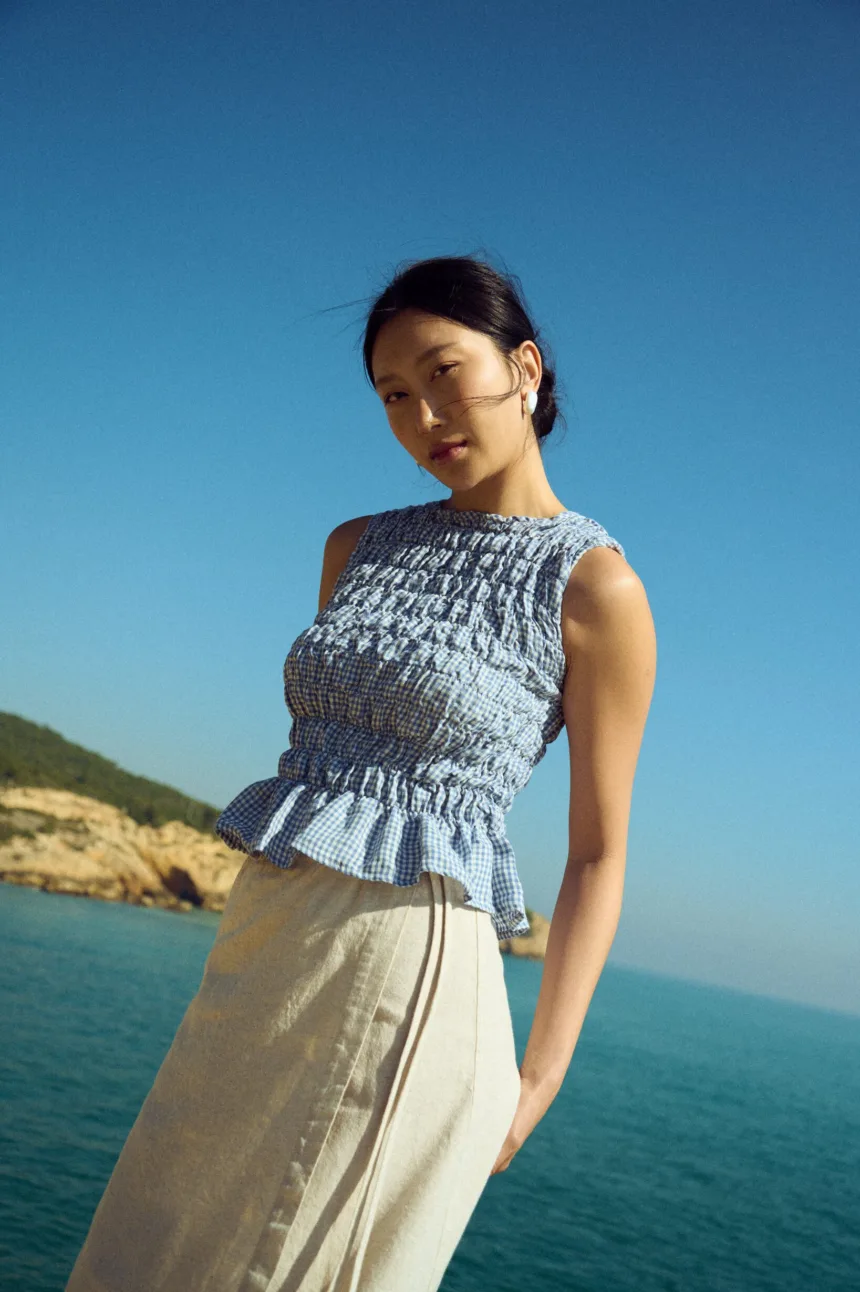 Blue gingham linen smocked top with gathered texture and soft peplum hem, paired with a natural linen cotton blend wrap skirt