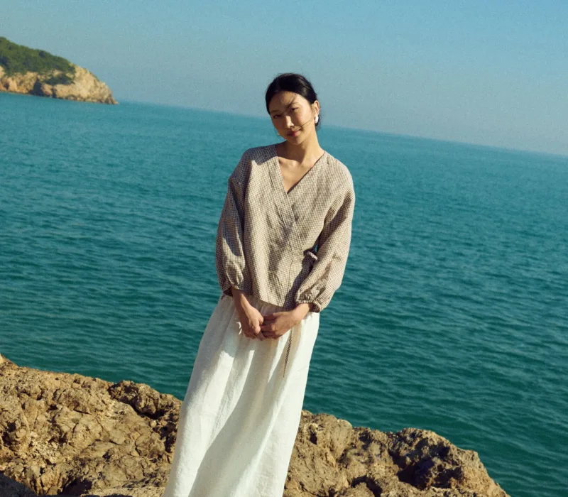 Brown gingham linen wrap top with soft V neckline and adjustable side tie, paired with a white linen skirt