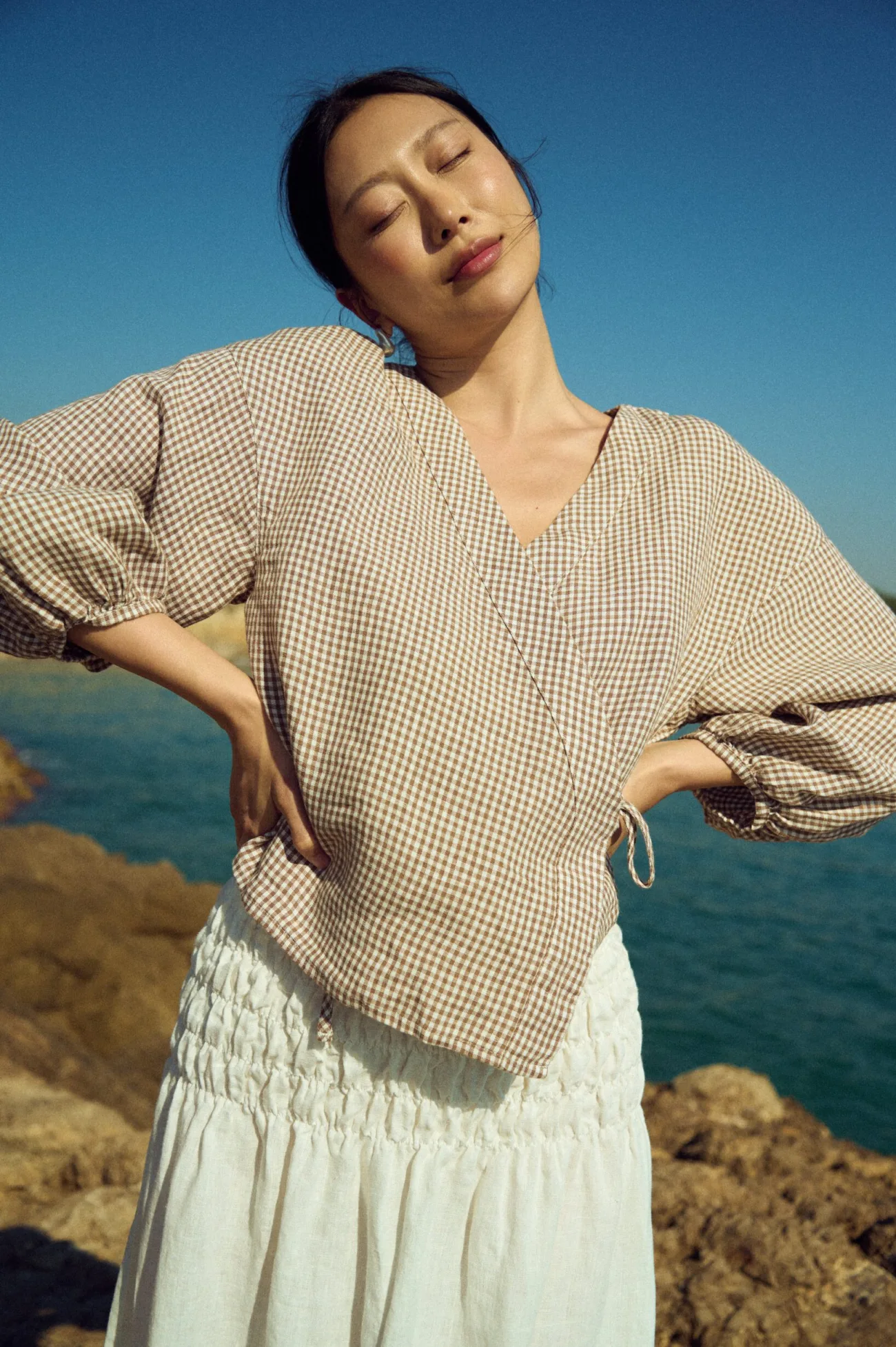 Brown gingham linen wrap top featuring a clean V-neckline and side tie fastening