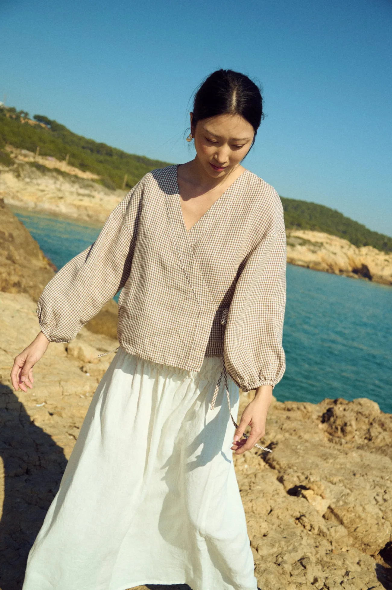 Brown gingham linen top with crossover front and adjustable waist tie, worn with a flowing white linen skirt
