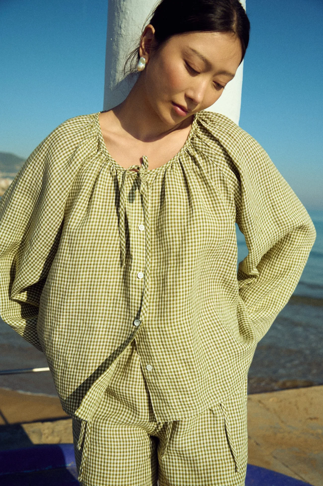 Moss green gingham linen blouse with softly gathered neckline and relaxed sleeves, worn with coordinating shorts