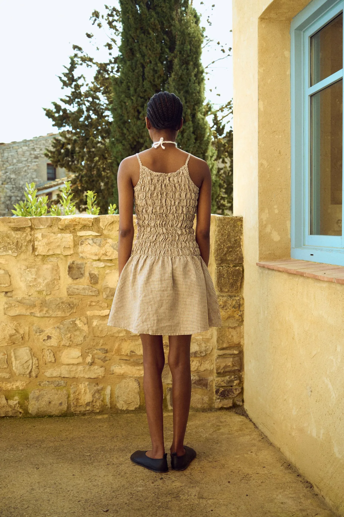 Back view of a brown gingham mini dress with a fully smocked bodice and thin straps