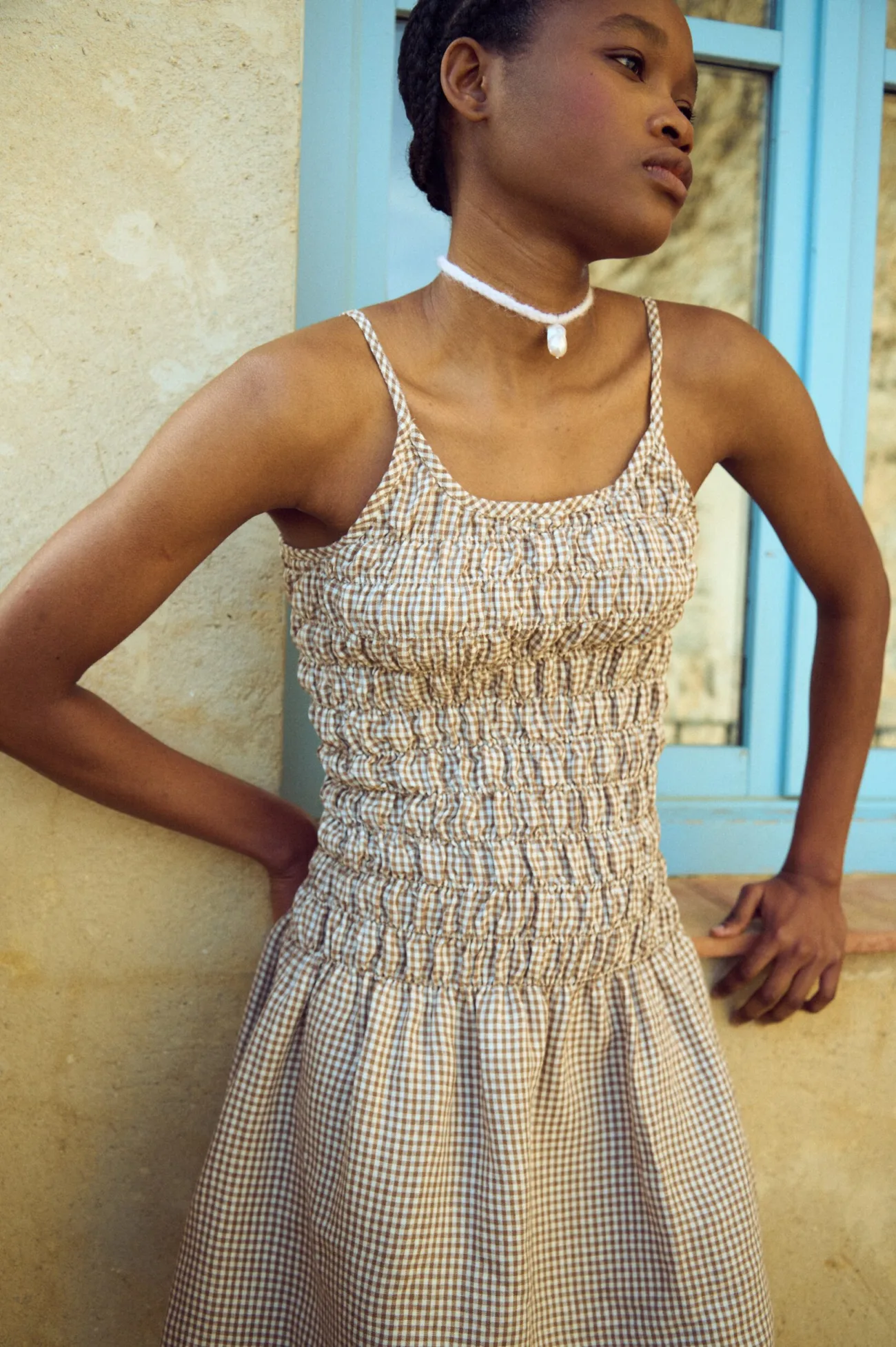 Model wearing a brown gingham linen dress with a smocked bodice and thin straps
