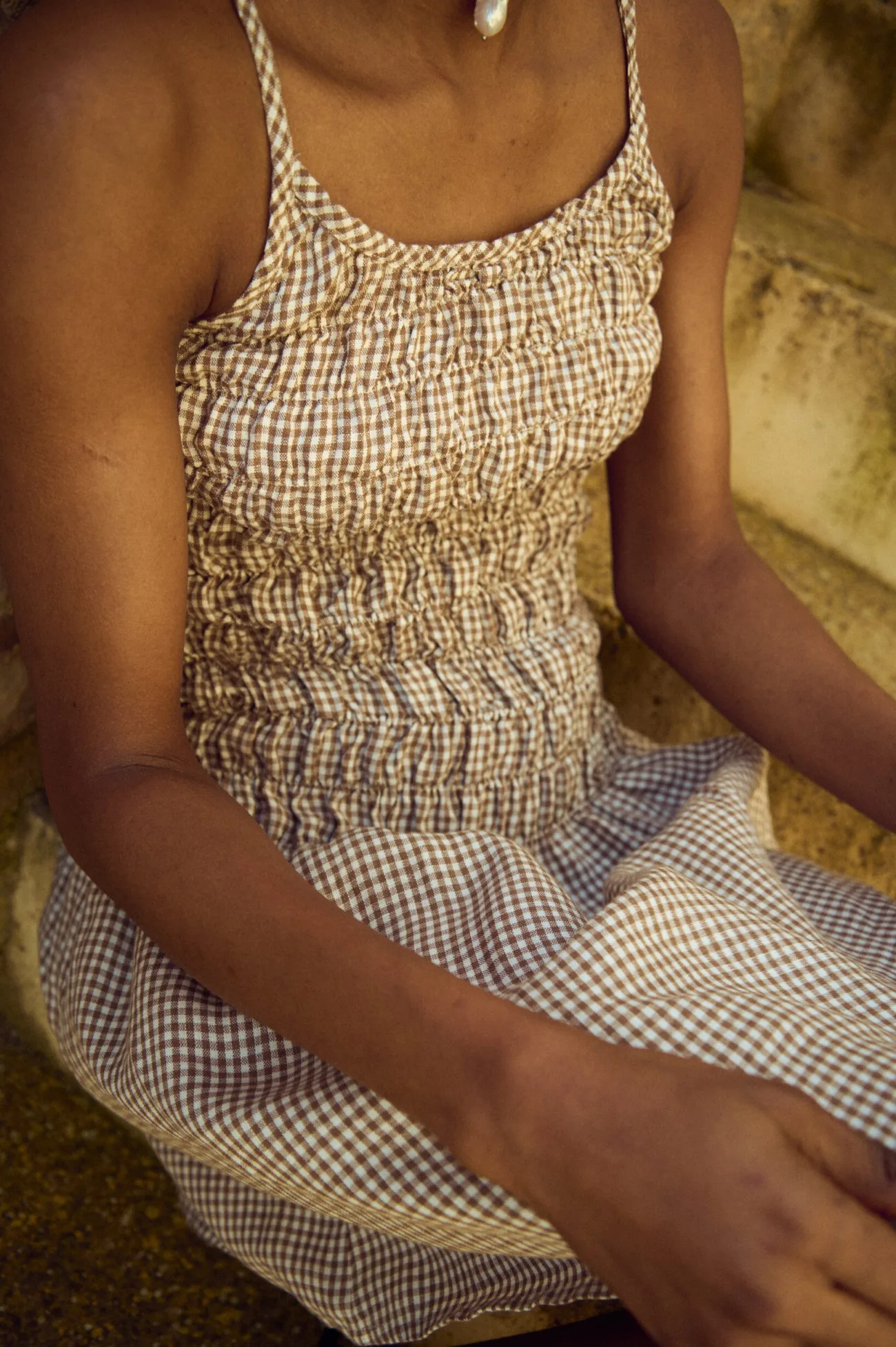 Close-up of a brown gingham mini dress featuring a smocked bodice and slender straps