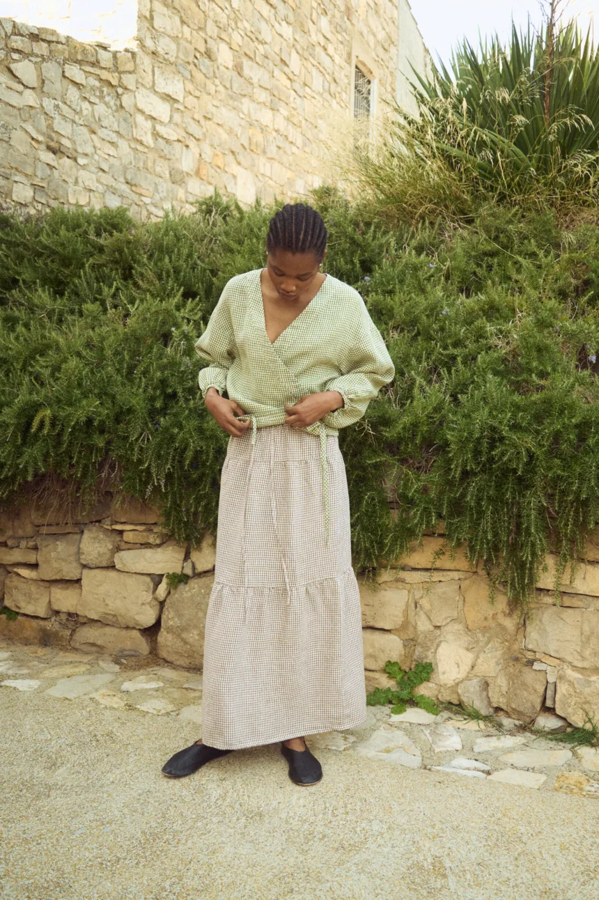 Brown gingham linen long skirt featuring a softly gathered lower panel and fluid drape, styled with a lightweight wrap blouse