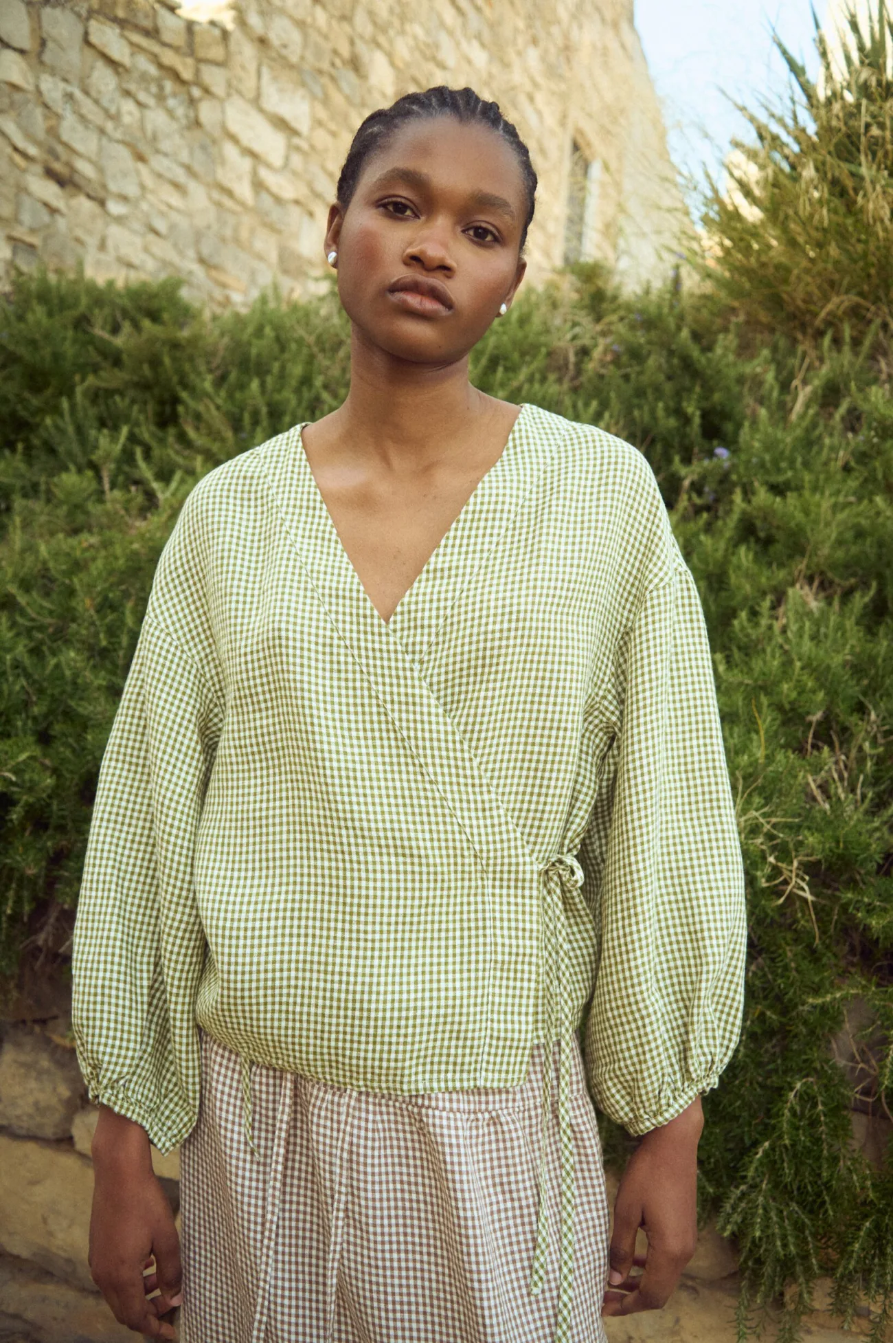 Green mini gingham linen wrap top with soft V neckline and adjustable side tie, paired with a brown gingham linen skirt