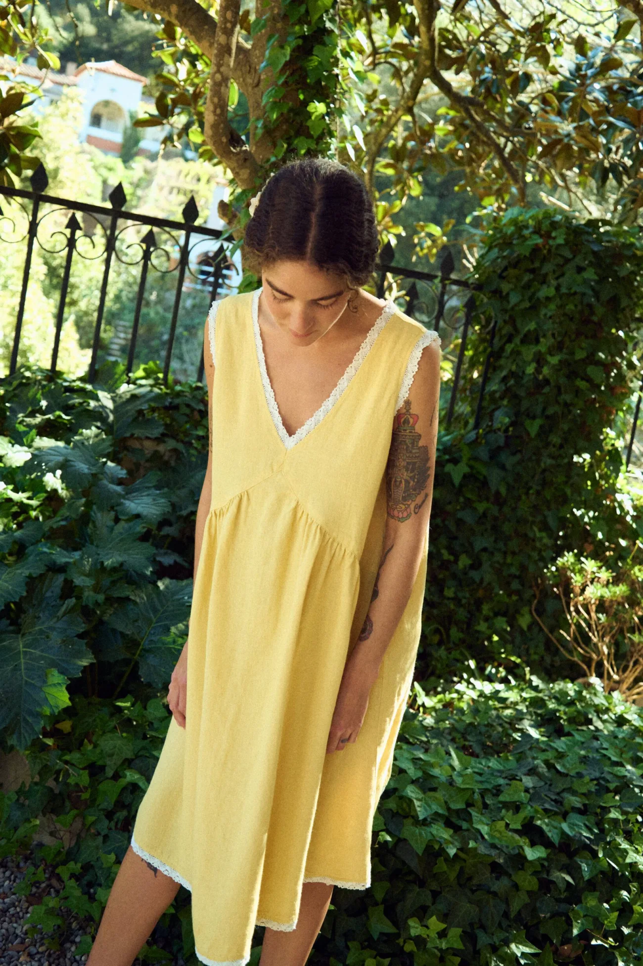 Angled front view of butter yellow linen sleeveless midi dress with lace-trim V-neck, armholes, and hem, and a softly gathered waist