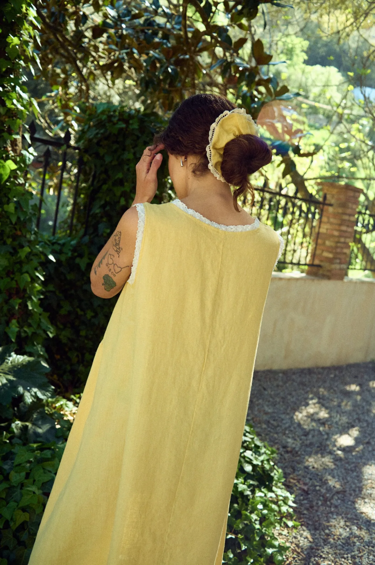 Back view of butter yellow linen sleeveless midi dress with lace-trim neckline and armholes, and a relaxed flowing fit
