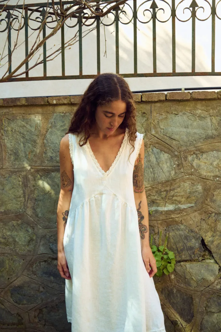 Close front view of milky white linen sleeveless midi dress with V-neck, lace-trim neckline, and softly gathered waist