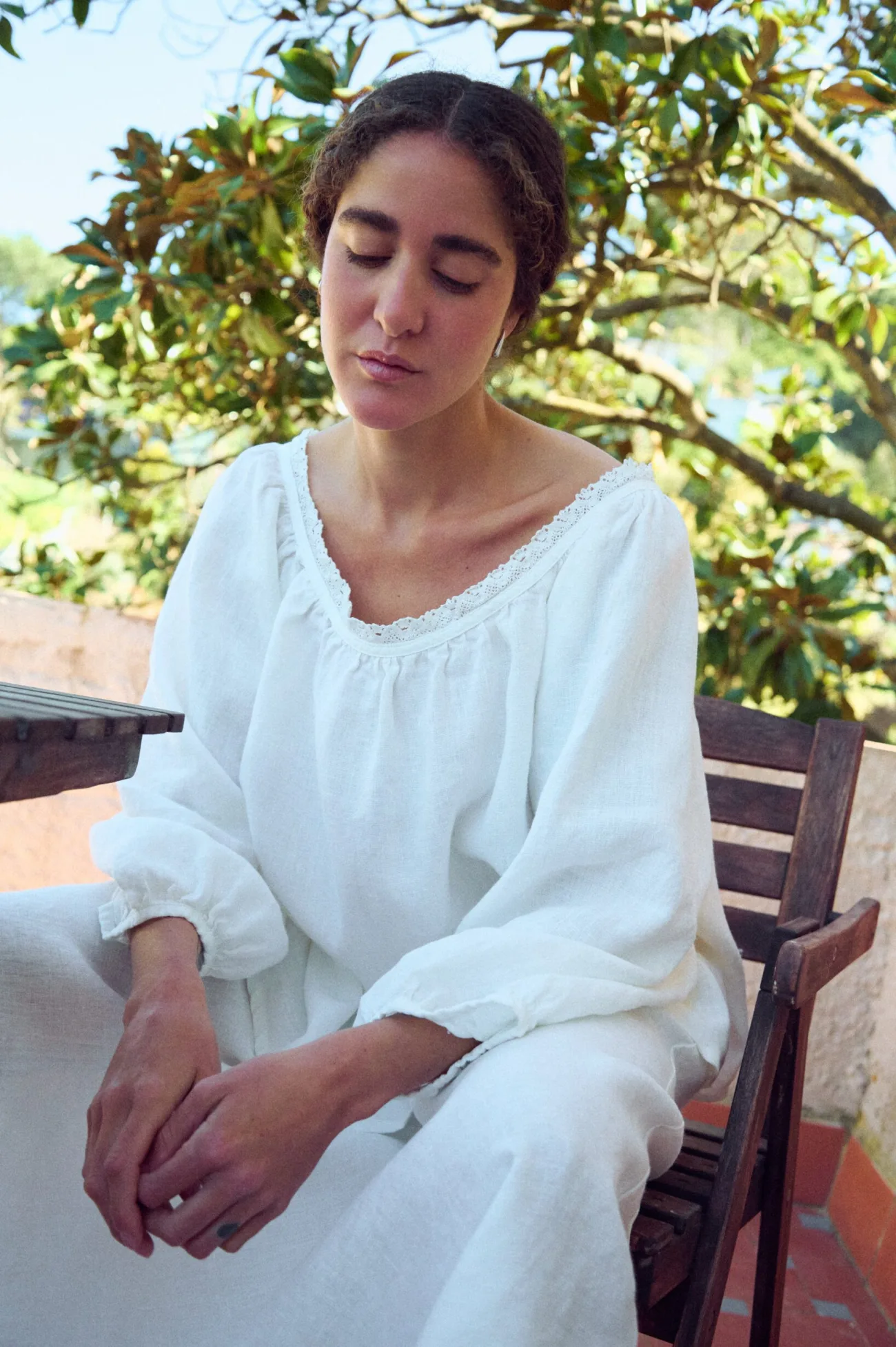 Close seated view of milky white linen blouse with lace-trim scoop neckline, gathered detail, and billowy sleeves