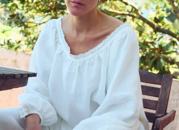 Close seated view of milky white linen blouse with lace-trim scoop neckline, gathered detail, and billowy sleeves