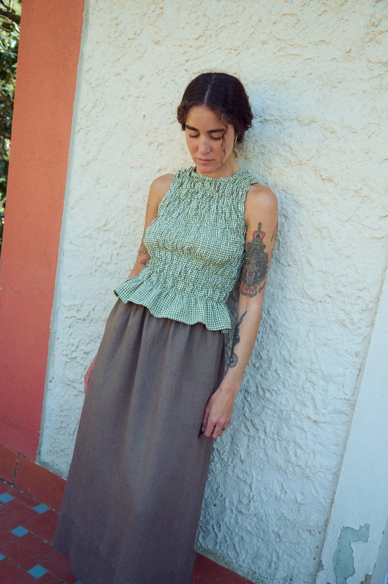 woman wearing smocked peplum linen top in moss green gingham paired with maxi brown skirt