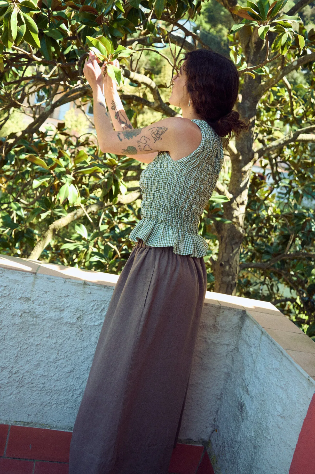 side view of smocked green gingham top with peplum flared hem styled with long brown linen skirt
