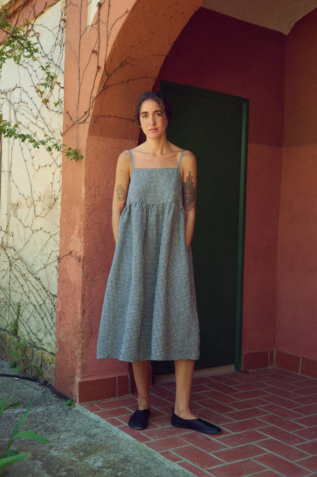 model posing in black gingham pinafore linen dress in midi length, with pockets and spaghetti straps